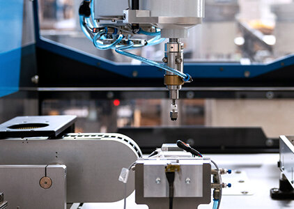 Detailaufnahme eines Blister-Automaten mit präzise geführtem Greifarm und mehreren pneumatischen Leitungen. Die Maschine ist für automatisierte Verpackungs- oder Bestückungsprozesse ausgelegt und befindet sich in einer industriellen Umgebung.