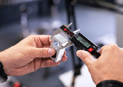 Nahaufnahme einer digitalen Schieblehre, mit der ein präzise gefertigtes Metallbauteil vermessen wird. Das Display zeigt den Messwert 29.57 mm – ein typischer Vorgang in der Qualitätskontrolle und Maßprüfung in der Fertigung.