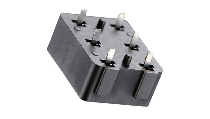  Schwarzes Kunststoffgehäuse mit sechs flachen Metallpins, vermutlich ein elektrischer Steckverbinder oder eine Buchse für eine elektronische Baugruppe. Das Bauteil ist freigestellt vor weißem Hintergrund dargestellt.