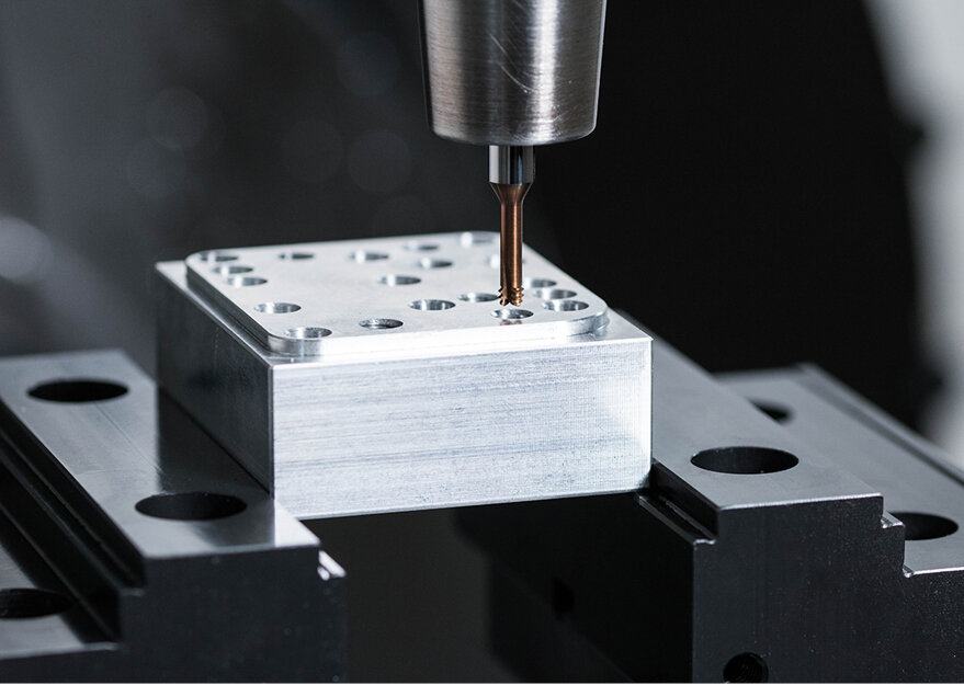 Nahaufnahme einer CNC-Fräsmaschine beim Bohren eines präzisen Lochbilds in einen Aluminiumblock. Das Werkstück ist fest eingespannt und wird mit hoher Genauigkeit bearbeitet – typisch für den Werkzeug- oder Formenbau.