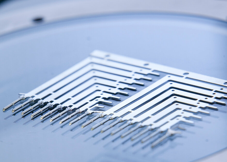 Präzise gestanzte Metallkontakte auf einem Trägerstreifen, ausgelegt für die Weiterverarbeitung in elektronischen Baugruppen. Die feinen Leitstrukturen zeigen typische Merkmale von Stanzgittern in der Verbindungstechnik oder Mikroelektronik.