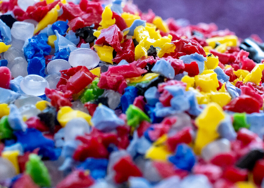 Nahaufnahme von buntem Kunststoffgranulat in verschiedenen Farben wie Rot, Gelb, Blau, Grün und Weiss, das als Rohmaterial für die Kunststoffverarbeitung verwendet wird. Die Granulatstücke sind unregelmäßig geformt und wirken recycelt.