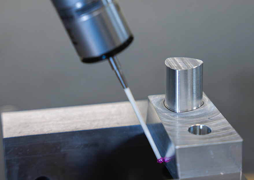 Nahaufnahme einer taktilen Messung mit einer Koordinatenmessmaschine, bei der ein metallisches Werkstück mit einem Messtaster präzise geprüft wird. Der Taster berührt die Kante eines gefrästen Bauteils mit zylindrischem Element.