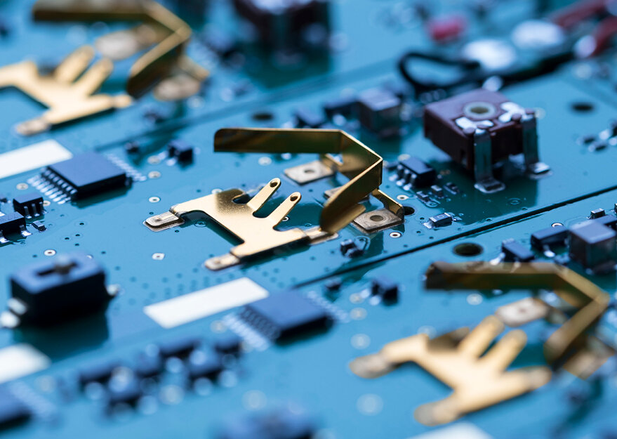 Nahaufnahme mehrerer goldfarbener Batteriehalter auf grünen Leiterplatten mit verschiedenen elektronischen Bauteilen. Die Halter sind mittig platziert und für den Kontakt mit Knopfzellen ausgelegt.