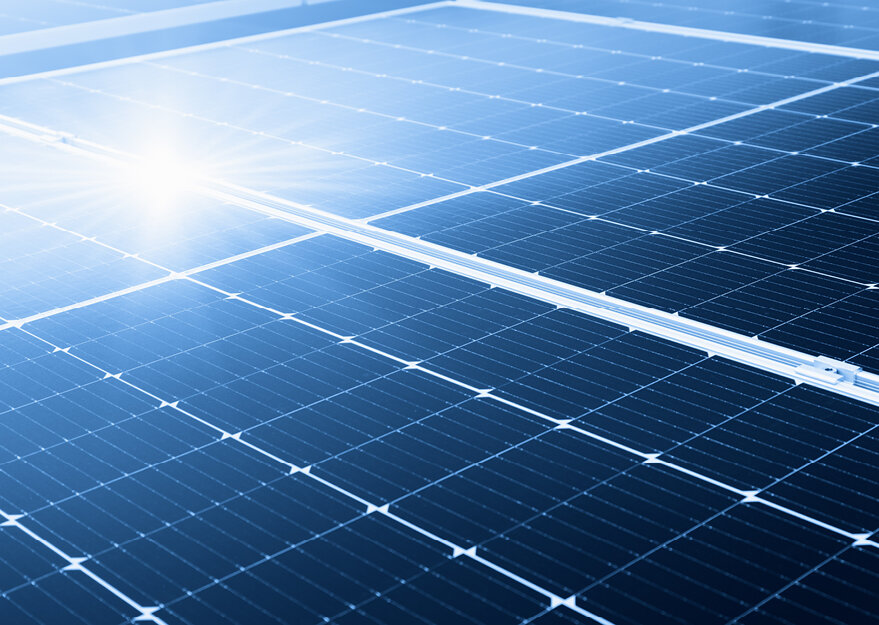 Nahaufnahme einer Photovoltaikanlage mit glänzenden Solarzellen unter direkter Sonneneinstrahlung, die Energie aus Sonnenlicht in Strom umwandeln. Die reflektierende Oberfläche der Module betont den technologischen Fokus auf nachhaltige Energiegewinnung.