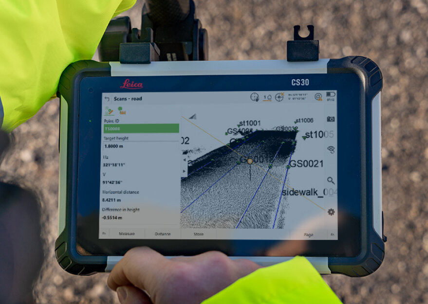 Ein Handgerät vom Typ Leica CS30 zeigt auf dem Bildschirm eine 3D-Vermessung eines Straßenabschnitts mit Punktwolken-Darstellung, Positionsdaten und Beschriftungen wie „sidewalk_002“. Die Hände einer Person in gelber Warnkleidung halten das Tablet bei der Vermessung im Freien.